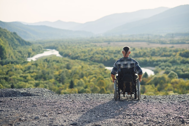 Young man in wheelchair enjoying fresh air in sunny day on the mountains