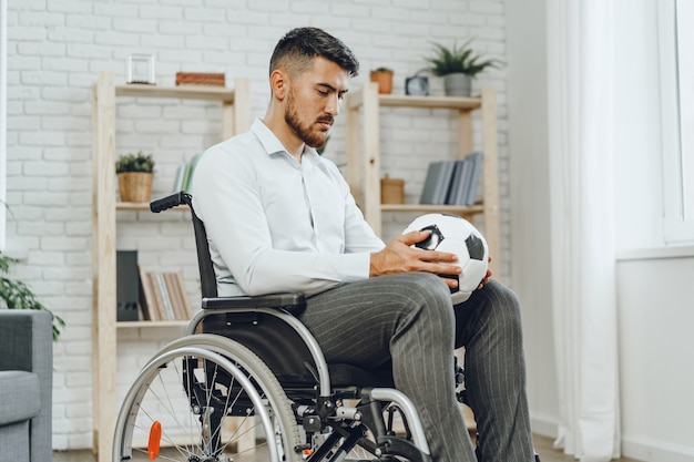 Young man in wheelchair holding football ball and thinking