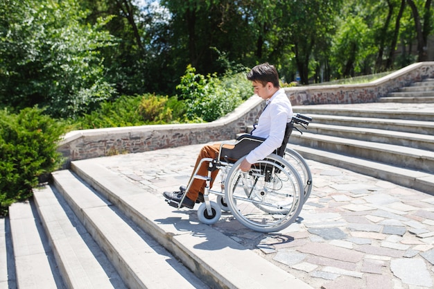 Photo a young man in a wheelchair who can not descend the stairs.