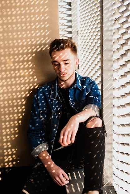 Photo young man while sitting by window against wall