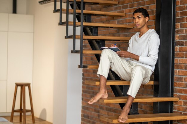 Young man in white clothes sitting on wooden stairs and making notes