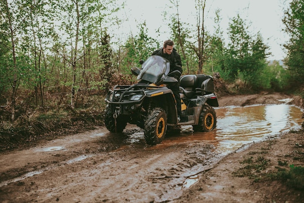 A young man in a white helmet rides through the woods on a Quad bike Extreme hobby A trip to ATV on the road from logs Quad Biking through the forest