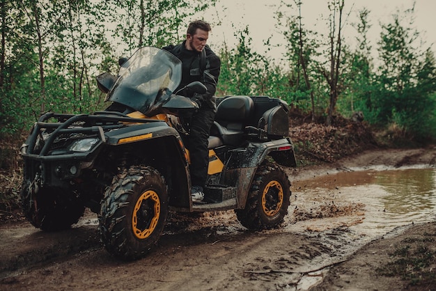 A young man in a white helmet rides through the woods on a Quad bike Extreme hobby A trip to ATV on the road from logs Quad Biking through the forest