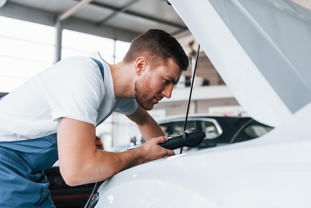 Foto il giovane in camicia bianca e uniforme blu ripara l'automobile