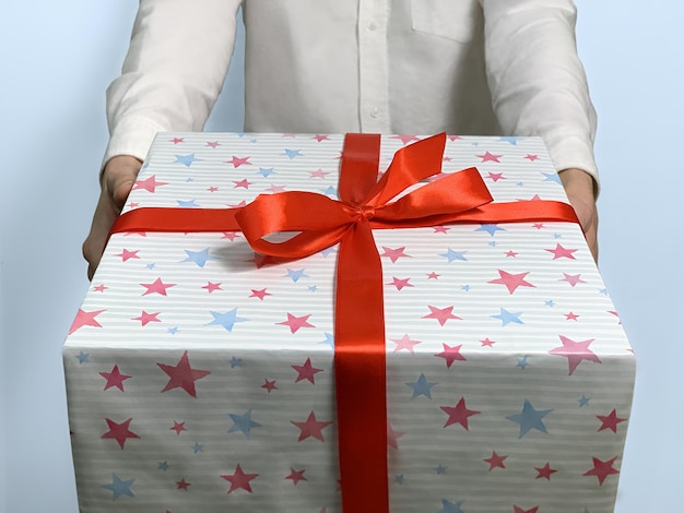 A young man in a white shirt gives big gift on blue background