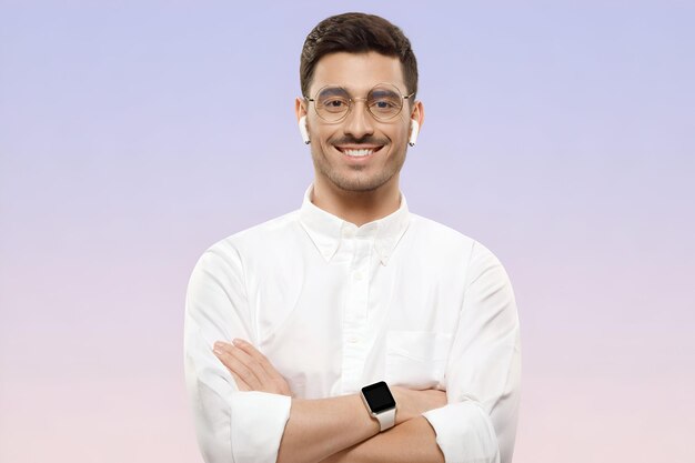 Young man in white shirt glasses and wireless earphones holding arms crossed with confident smile