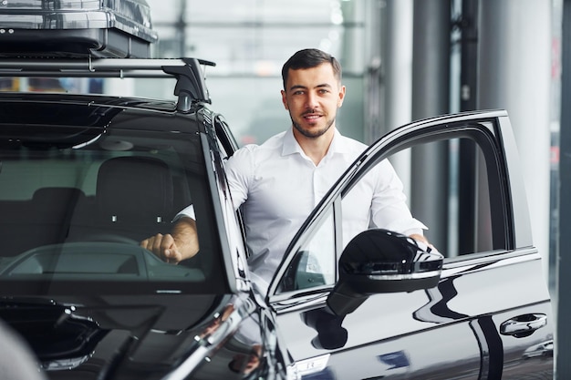 Young man in white shirt is indoors with modern new automobile