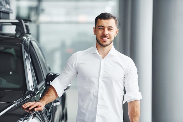 Young man in white shirt is indoors with modern new automobile