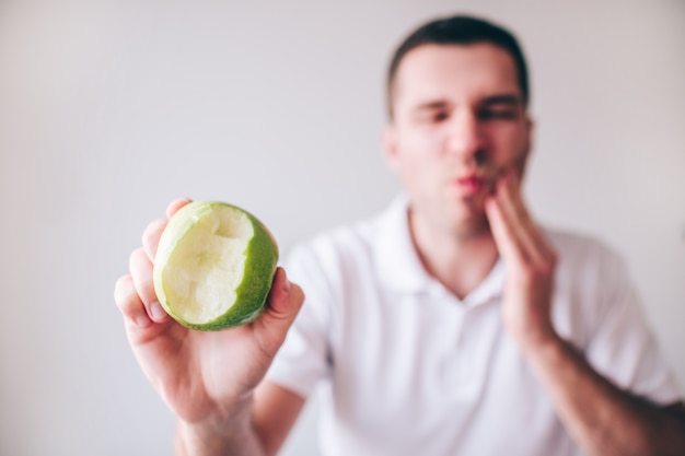 Young man in white shirt isolated over blurred defocused background. Guy suffer from pain tooth pain and ache.