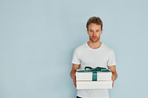 Young man in white shirt standing against wall and holds gift box