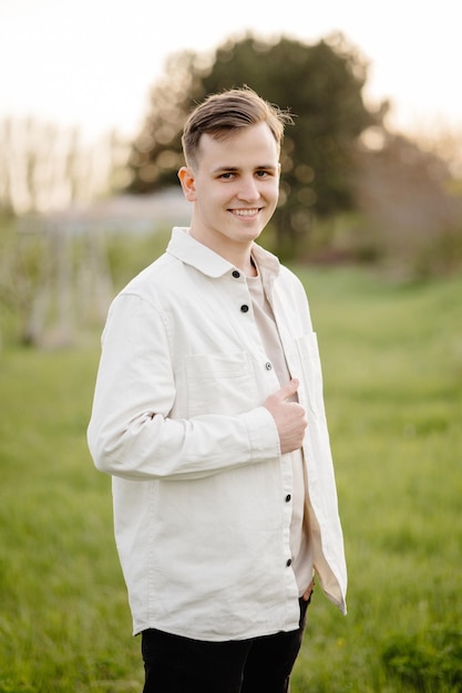 Молодой человек в белой рубашке стоит в поле и улыбается в камеру.