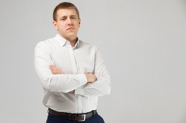 Young man in white shirt stands on white with folded arms on chest