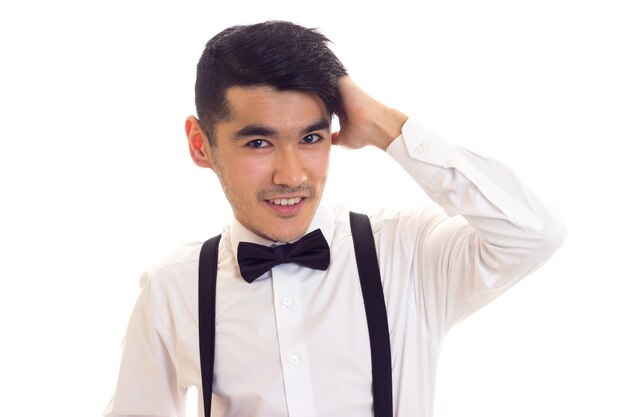 Young man in white shirt with black bowtie and black suspenders on white background in studio