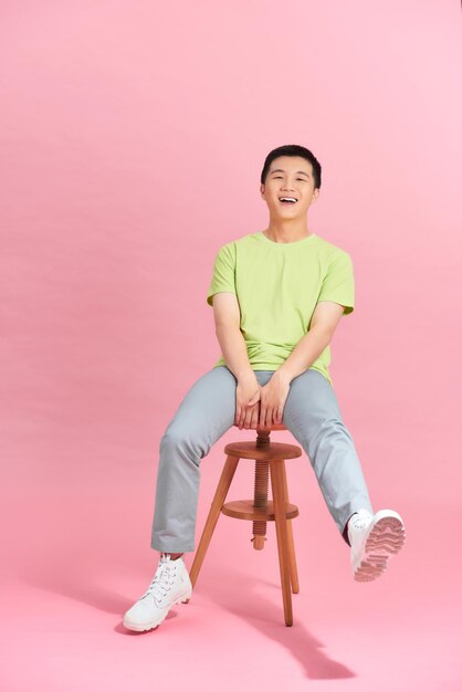 A young man in a white T-shirt is sitting on a high chair.