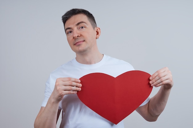 彼の手に紙のハートを持つ白いTシャツの若い男