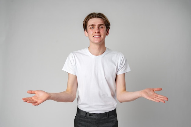 Young man in white tshirt gesturing with open arms against a plain background