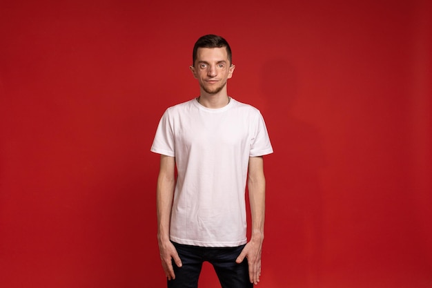 A young man in a white Tshirt stands against a red background and smiles