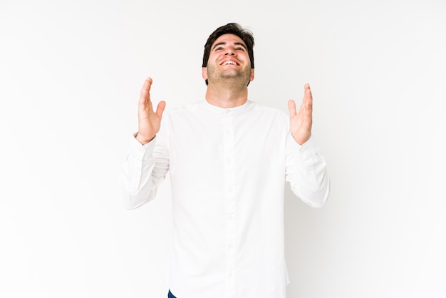 Young man on white wall laughs out loudly keeping hand on chest.