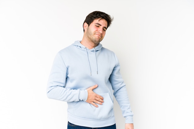 Young man on white wall touches tummy, smiles gently