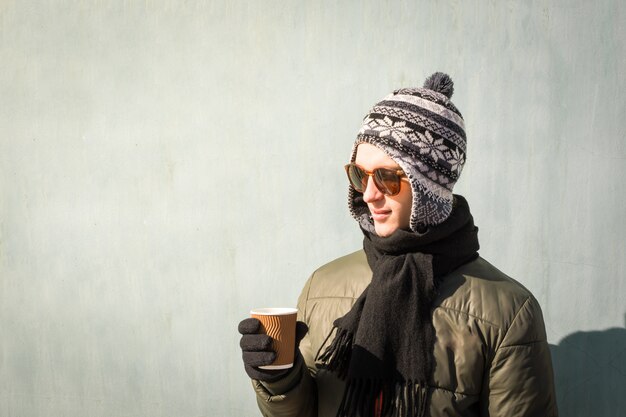 冬の服の若い男は一杯のコーヒーを保持しています。