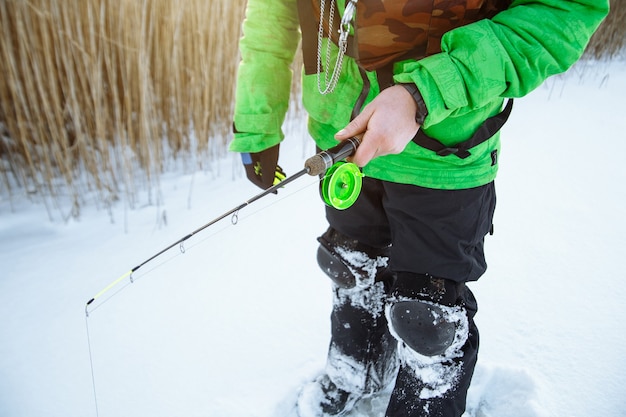 Young man on a winter fishing trip on a snowy lake fishes on a fishing rod