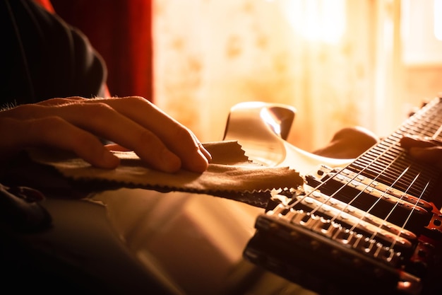 Photo a young man wipes dust off an electric guitar closeup sun rays