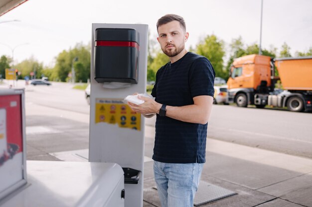 ガソリンスタンドで車に給油した後、濡れたナプキンで手を拭く若い男性