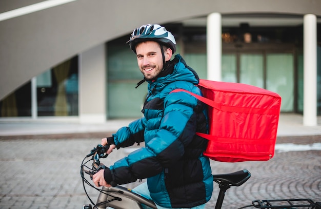 写真 食品配達用のバックパックと自転車保護ヘルメットを持つ若い男。宿題、自転車に乗る、ピザの配達