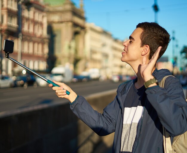 写真 携帯電話を持つ若い男は大都市の通りで、手を振って