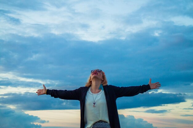 Photo young man with arms outstretched standing against sky