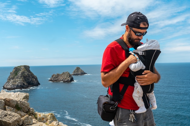 フランスの3つの有名な小島、フランスのブリタニーのクロゾン半島にあるペンヒルポイントで海を見ているバックパックと赤ちゃんを持つ若い男