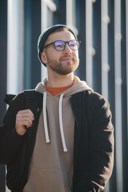 A young man with a backpack and casual clothes on the background of an office building