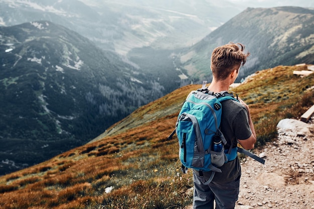 young man with backpack hiking in a mountains actively spending summer vacation