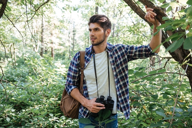 Young man with backpack near the tree looking away