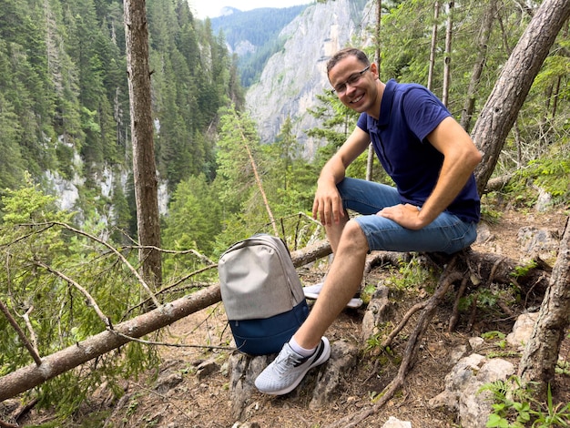 Young man with backpack resting in forest in mountains