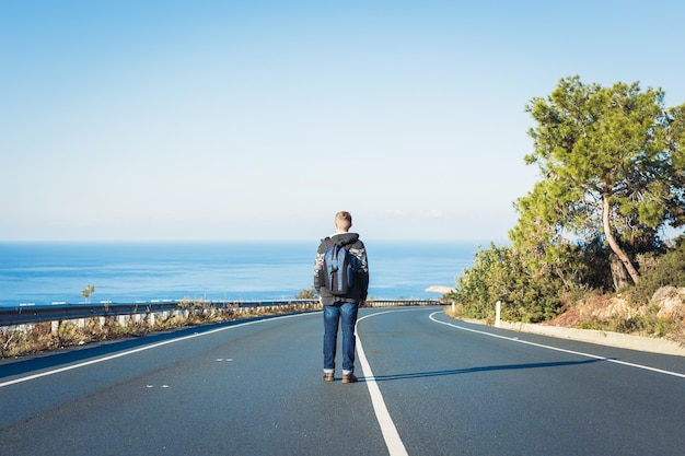 Il giovane con uno zaino cammina da solo su una strada. concetto di viaggio