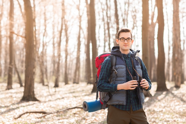 Young man with backpack and with a binocular in his hands, hiking in the forest