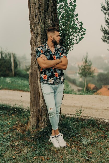 Young man with beard and flowered shirt posing in nature