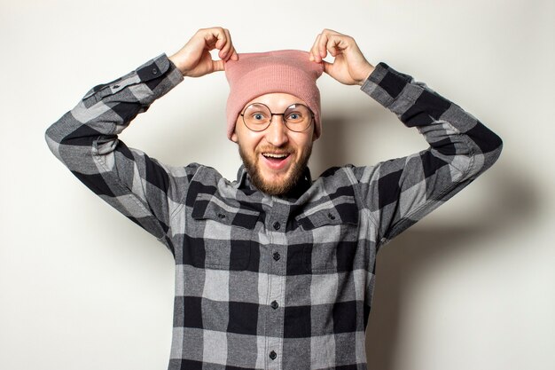 Young man with a beard in a hat, a plaid shirt takes off his
hat on an isolated white.