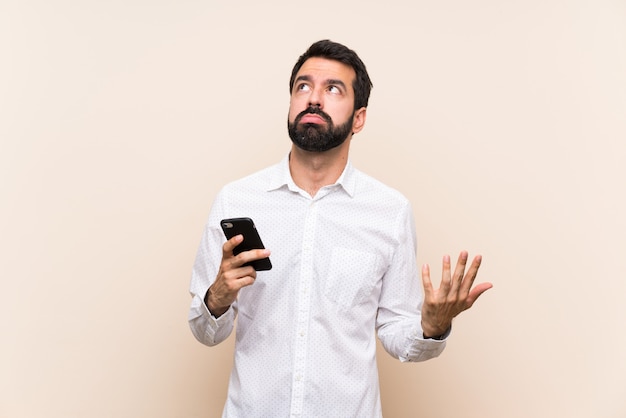 Молодой человек с бородой держит мобильный телефон разочарован плохой ситуацией