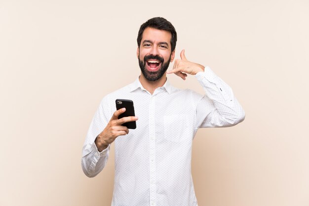 Young man with beard holding a mobile making phone gesture. Call me back sign