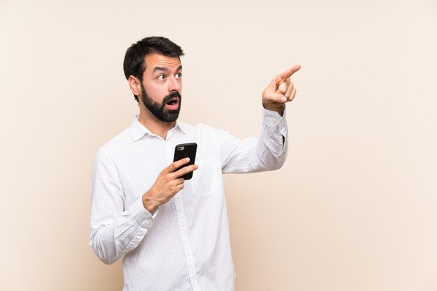 Young man with beard holding a mobile pointing away