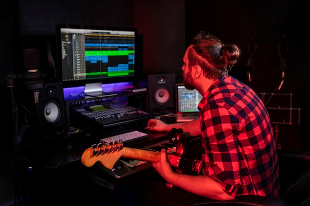 Young man with beard is playing guitar in the stereo studio on the radio to record his new song