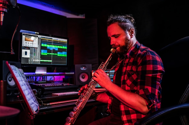 수염을 가진 젊은 남자가 그의 새로운 노래를 녹음하기 위해 스튜디오에서 악기를 연주하고 있습니다.