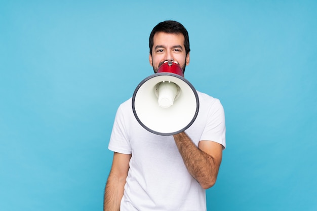 Young man with beard  over isolated blue background shouting through a megaphone