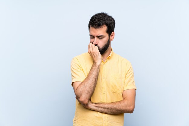 Giovane con la barba sopra il blu isolato che ha dubbi