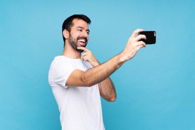 Young man with beard  over isolated blue making a selfie