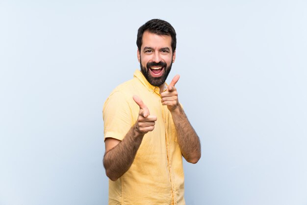 Young man with beard over isolated blue  pointing to the front and smiling