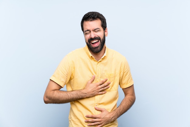 Young man with beard over isolated blue   smiling a lot