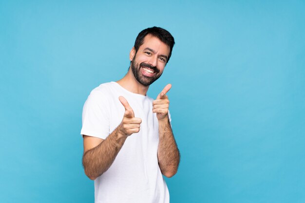 Young man with beard  over isolated blue wall pointing to the front and smiling